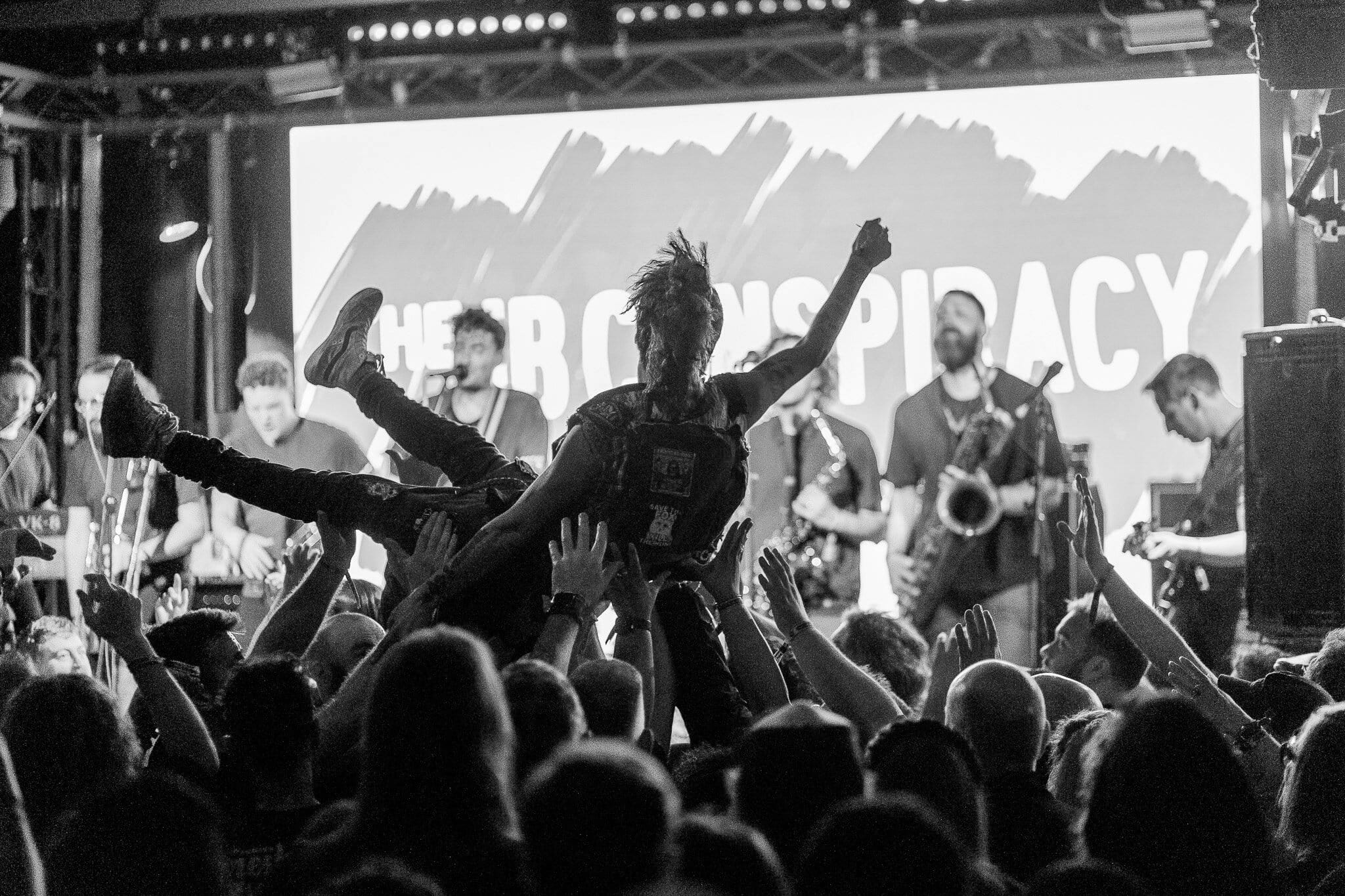 A crowd surfer held aloft in front of a ska-punk band on stage at Manchester Punk Festival