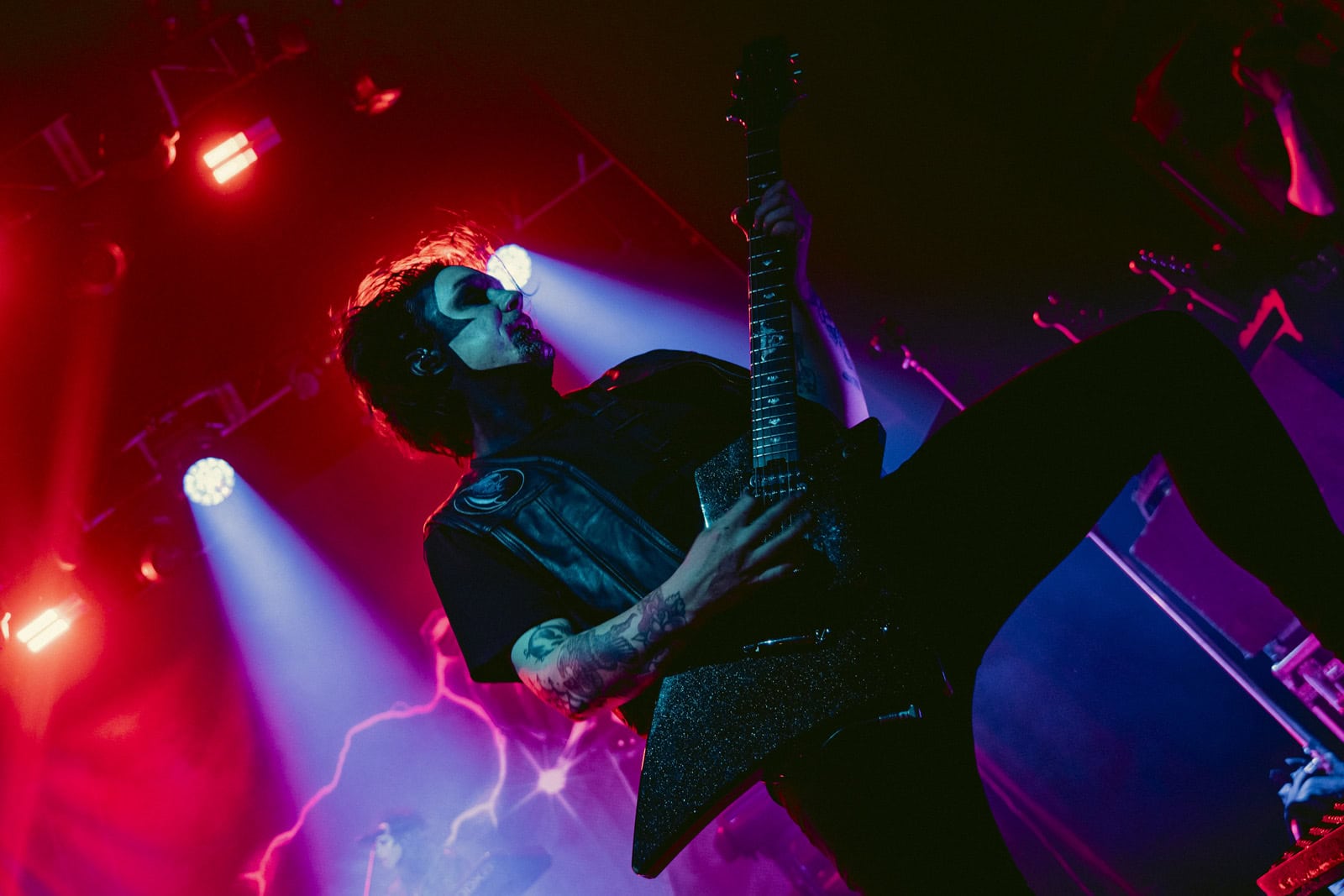 A Creeper guitarist leaning back with his guitar under red and blue lights