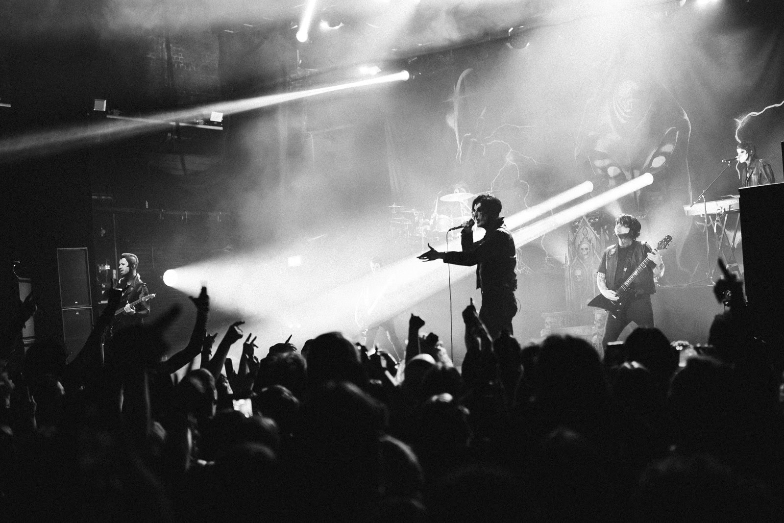 Black-and-white shot of Creeper on stage through haze above a crowd of raised hands